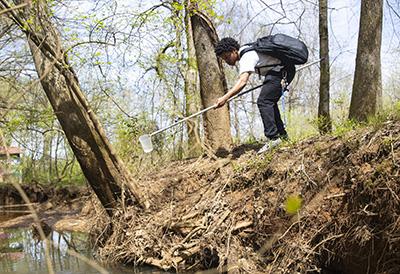 student beside creek taking water sample